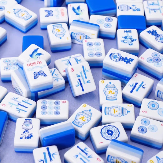 A scattered pile of classic blue and white style Mahjong tiles showing the triple-layer blue gradient backing, butterfly winds, and detailed ginger jar craks.