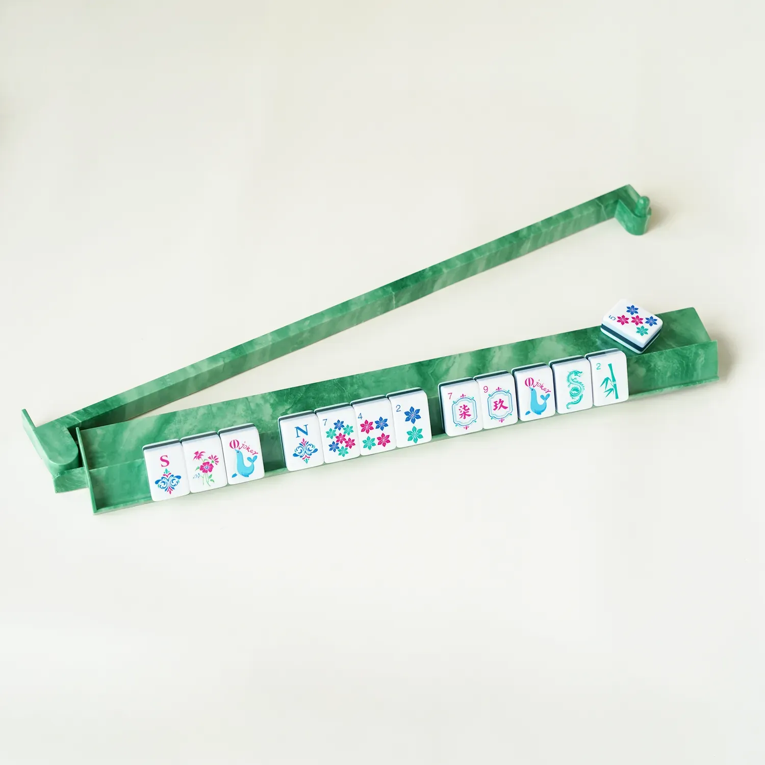 A single jade green mahjong rack holding a neat row of American mahjong tiles with the pusher extended, demonstrating game night play.
