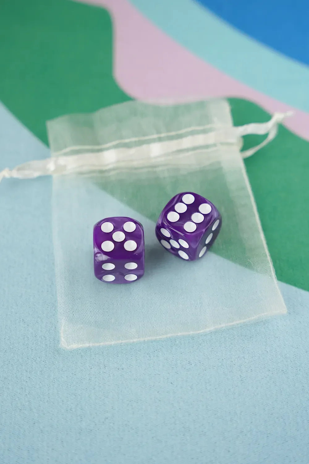 A pair of orchid purple 5/8 inch marbled acrylic mahjong dice with white pips in a sheer organza pouch.