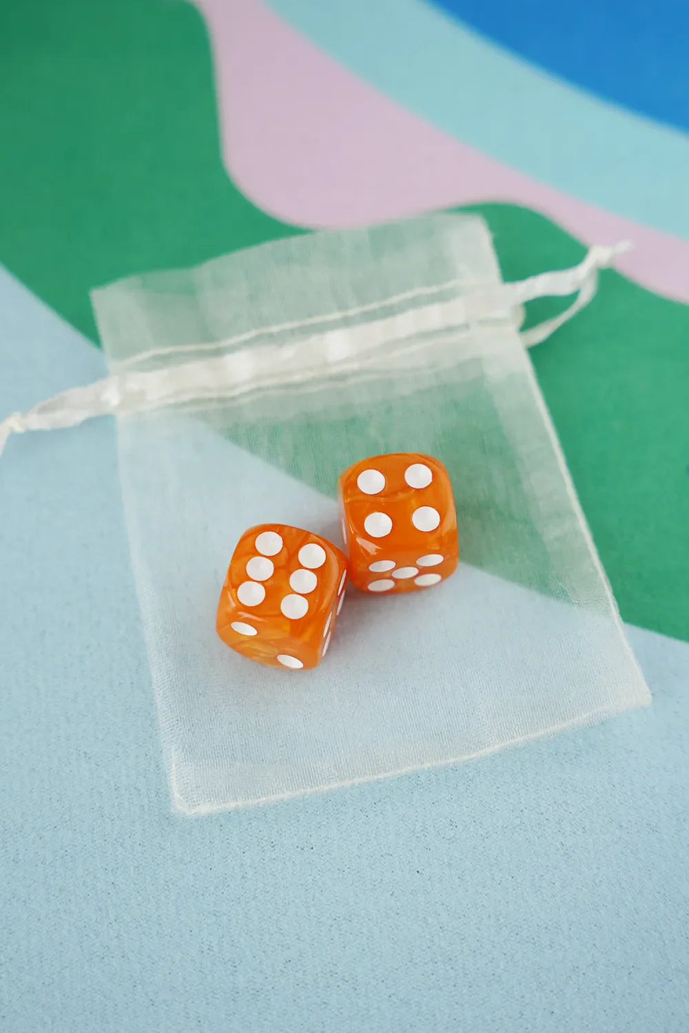 A pair of tangerine orange 5/8 inch marbled acrylic mahjong dice with white pips in a sheer organza pouch.